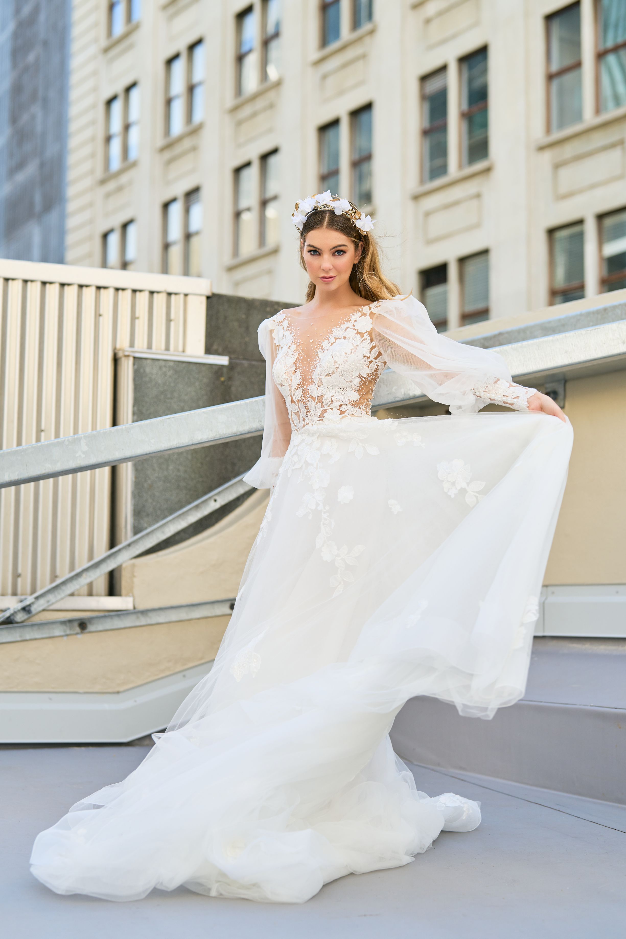 Rubi wedding dress with floral detailing on décolletage and skirt. Sheer sleeves add a delicate touch. Plunging v-neckline and A-line silhouette create an elegant and romantic look that makes you appear to be floating down the aisle.