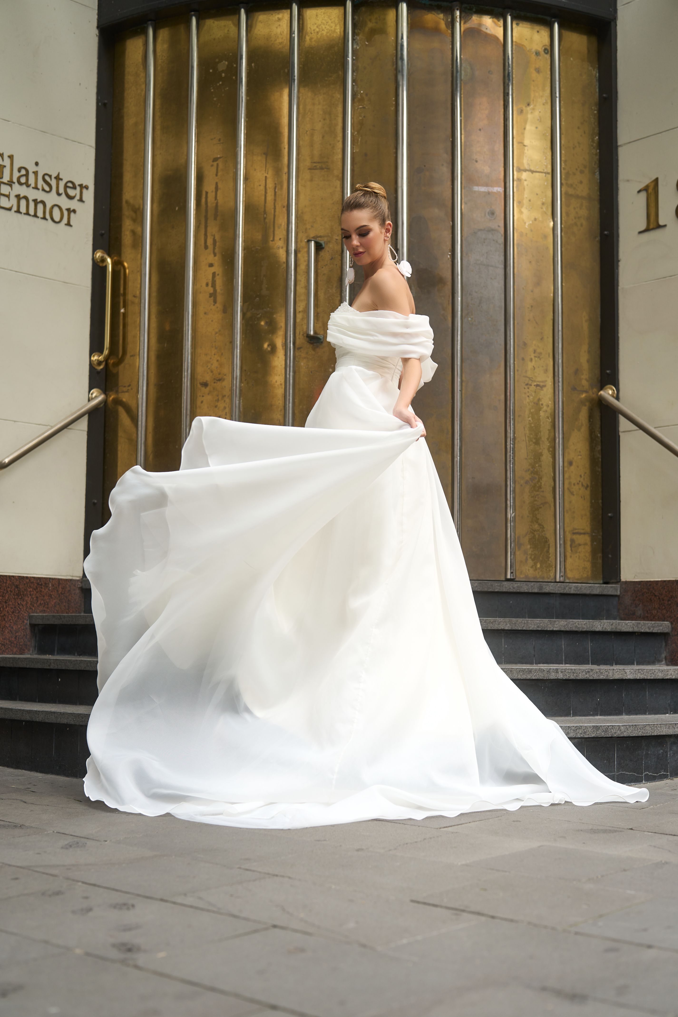 Rhianna wedding dress in sheer Organza fabric with off-the-shoulder pleated band and A-line silhouette. Wide waistband and light skirt with chapel train. High split adds a modern touch and ease of movement for walking and dancing all day.