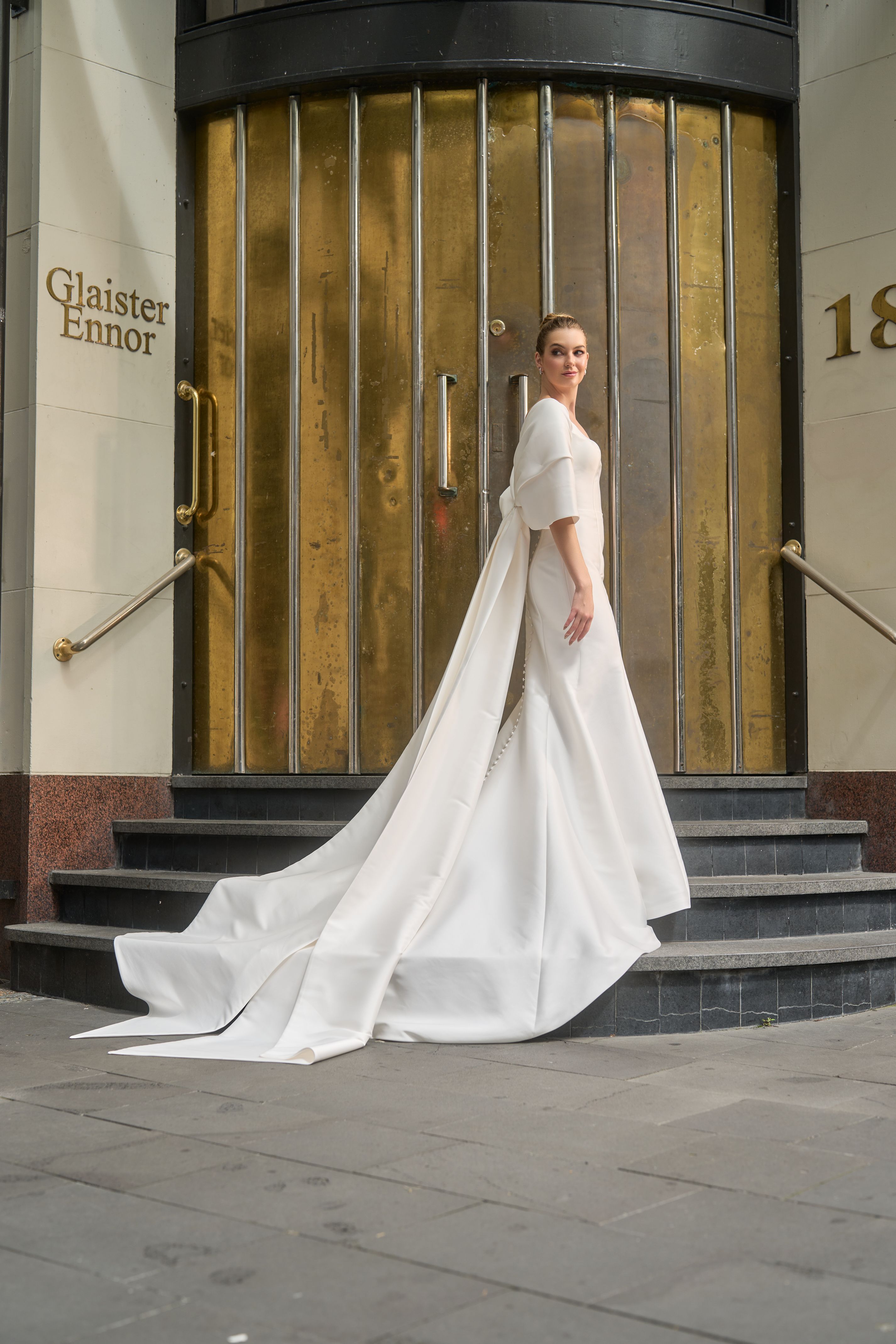 Ivory mikado minimalist gown with rouched tulle separate sleeves. Oversized bow that wraps over arms.