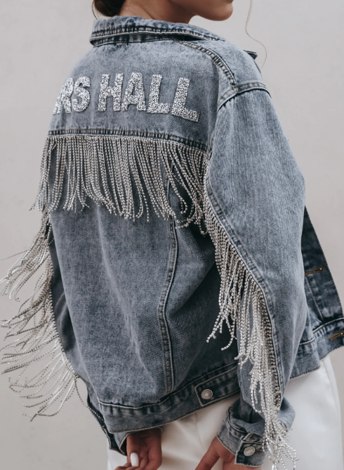 Side view of blue denim jacket with diamante fringe down arms and across back. Lettering reading 'MRS. HALL'