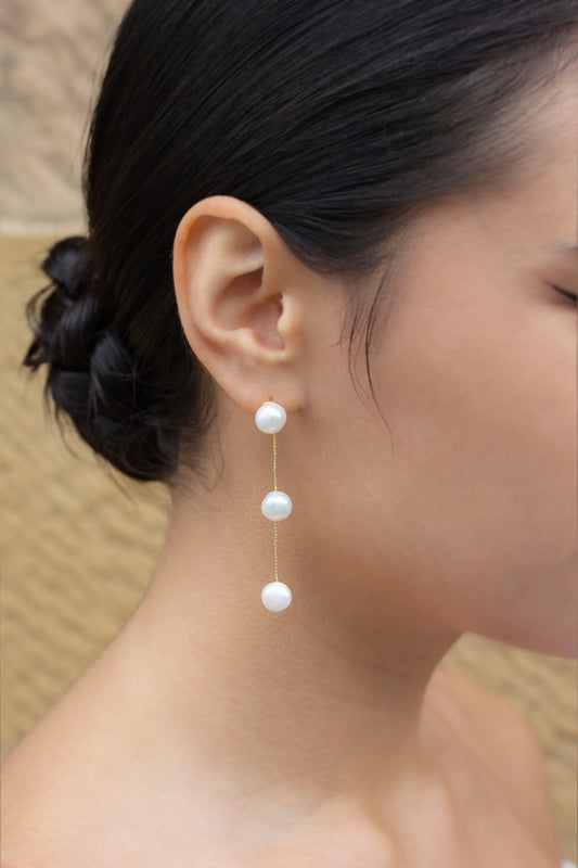Image of model wearing earring with three freshwater pearls hanging in a row joined by gold chain.